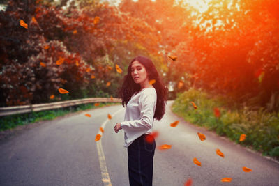 Portrait of young woman standing on road during autumn