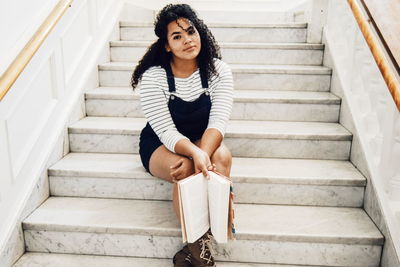 Portrait of young woman with book sitting on steps