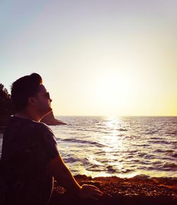 Man wearing sunglasses while standing by sea against sky during sunset