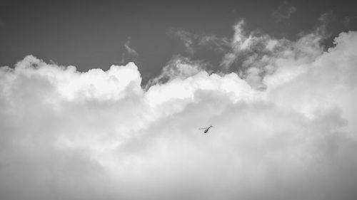 Low angle view of helicopter flying against cloudy sky