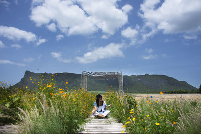 Rear view of women sitting on flowering plants against sky