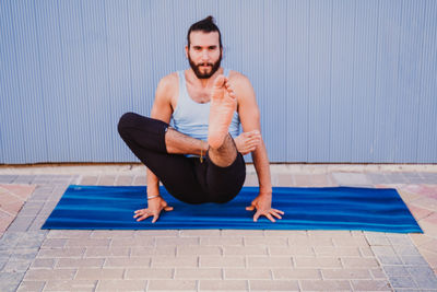 Full length of man performing yoga on exercising mat against wall