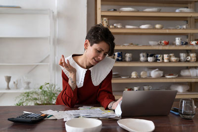 Focused young woman ceramic studio owner analyzing bills and receipts, doing pottery cost analysis