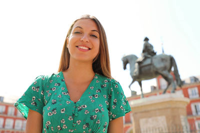 Portrait of smiling young woman standing against clear sky