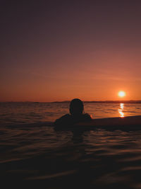 Silhouette man swimming in sea against sky during sunset