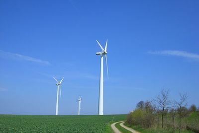 Low angle view of wind turbines on field against blue sky