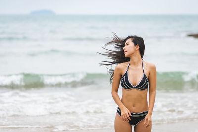 Young woman tossing hair standing at shore of beach
