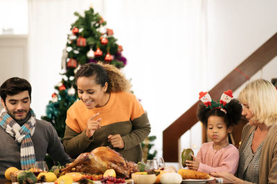 People sitting by food on table against christmas tree