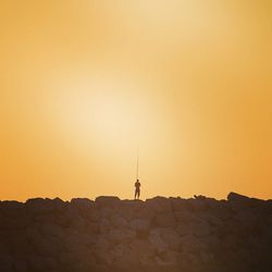 Silhouette man standing on rock against sky during sunset