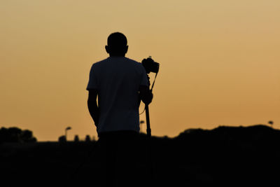 Rear view of silhouette man standing against sky during sunset