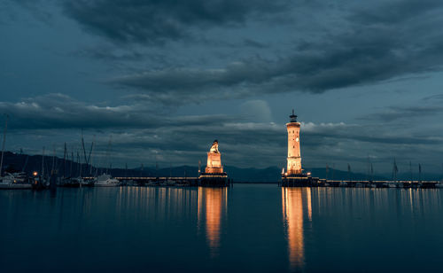 Reflection of lighthouse on sea against cloudy sky