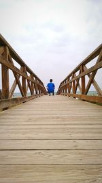 Rear view of man sitting on pier over sea against cloudy sky