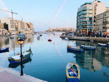 Sailboats moored on canal amidst buildings in city against sky