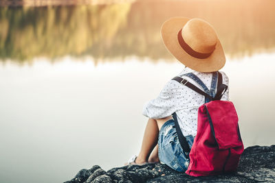 Rear view of boy sitting on rock looking at lake