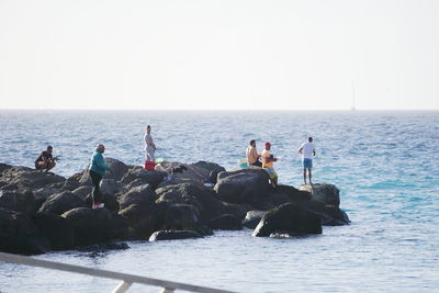 People standing on rocks by sea against clear sky