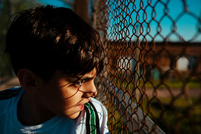 Close-up f boy looking through chainlink fence