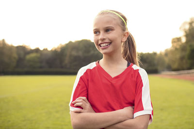 Happy female athlete looking away standing with arms crossed on soccer field