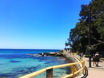 People by sea against clear blue sky