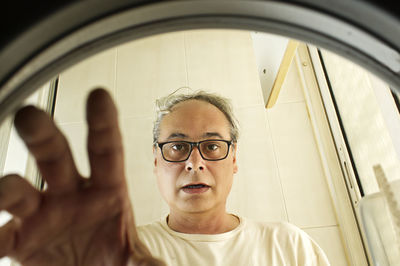 Mature man taking clothes out of the washing machine seen from inside