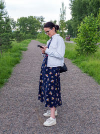 Middle-aged woman is using smartphone in urban park. full-length portrait.