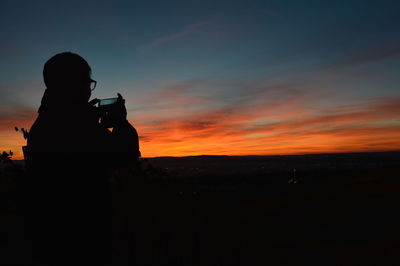 Silhouette woman photographing against sky during sunset