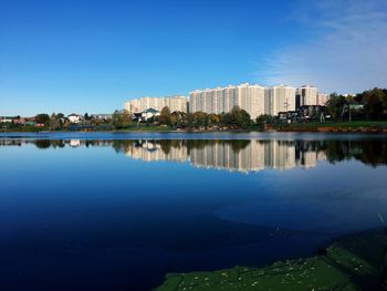 Scenic view of lake by buildings against blue sky
