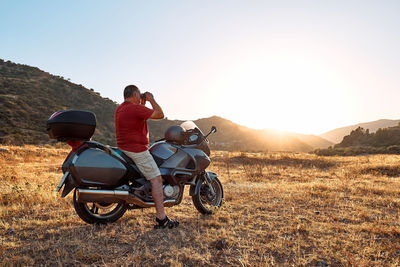 On the road.tourist man traveling on motorcycle, looking through binoculars at mountains in sunset