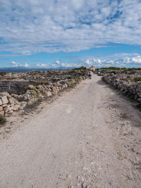 Dirt road amidst land against sky
