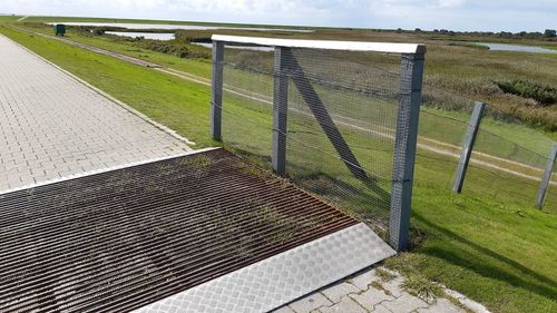 Fence on field by road against sky