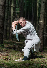 Full body man in traditional clothes practicing sword stance during kung fu training in forest