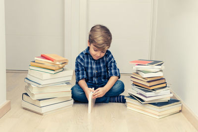 Small kid learning while sitting on the floor among heap of books.
