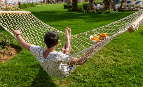 Rear view of man holding plate of fruits in hammock