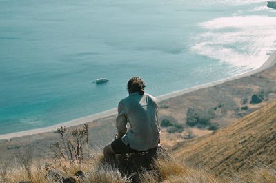 Rear view of man sitting on shore
