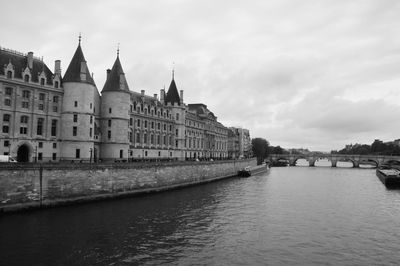 View of buildings by river against cloudy sky