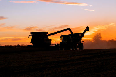 Silhouette combine harvester on land against sky during sunset