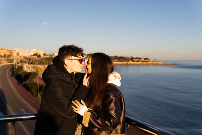 Young couple in the midst of an affectionate kiss on an oceanfront balcony