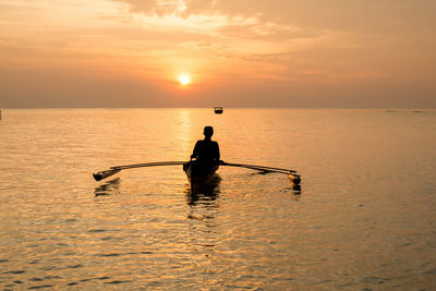 Silhouette man in sea against sky during sunset