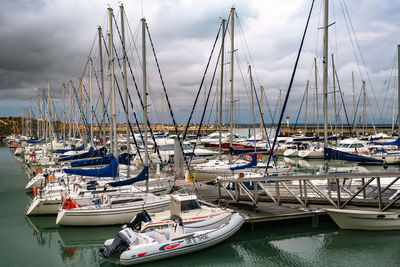 Sailboats moored on harbor against sky