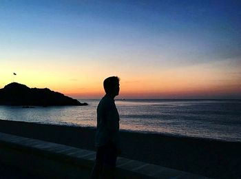 Silhouette man standing on beach against clear sky during sunset