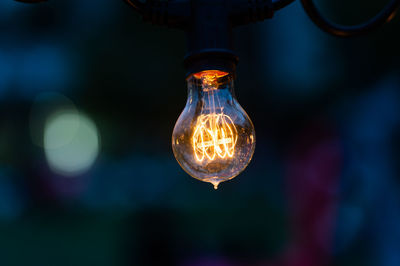 Close-up of illuminated light bulb hanging outdoors