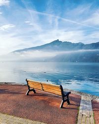 Empty bench by lake against sky