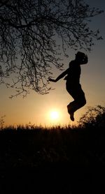 Silhouette man jumping on field against sky during sunset