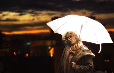 Mid adult woman standing with illuminated umbrella against sky during sunset