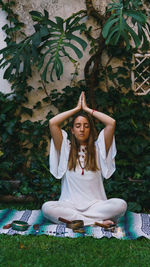 Full length of young woman meditating while sitting outdoors