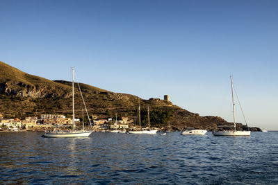 Sailboats in sea off headland  against clear blue sky