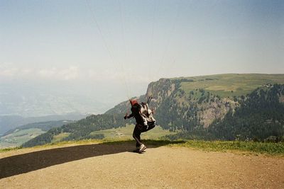 Man holding ropes while paragliding on mountain against sky