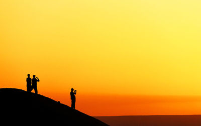 Silhouette people standing on sand dune at erg chebbi desert against sky during sunset