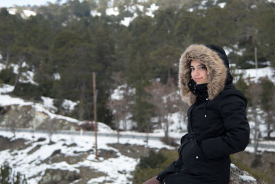 Portrait of young woman standing against trees during winter