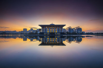 Buildings by lake at sunset