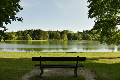 Bench in park by lake against sky